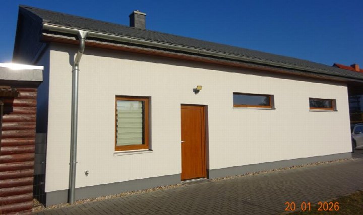 Seitenansicht eines Einfamilienhauses mit Holztür, Fenstern und grauem Dach unter klarem Himmel in Doberschütz, Heidecker Weg 67