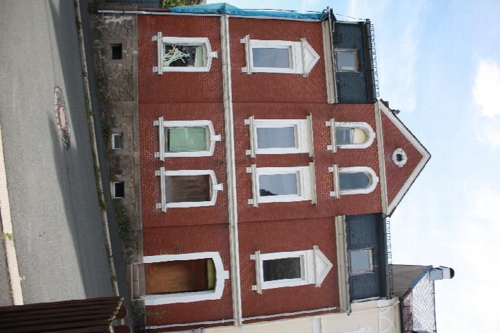 Fassade eines mehrstöckigen Backsteinhauses mit weißen Fensterrahmen und Eingangstür, Bergstraße 1, Helmbrechts
