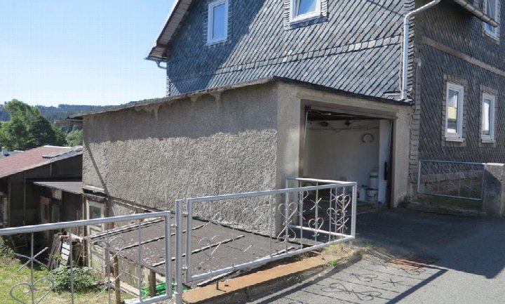 Garage mit offener Tür an einem Einfamilienhaus, Betonwand, Metallgeländer und Asphaltzufahrt