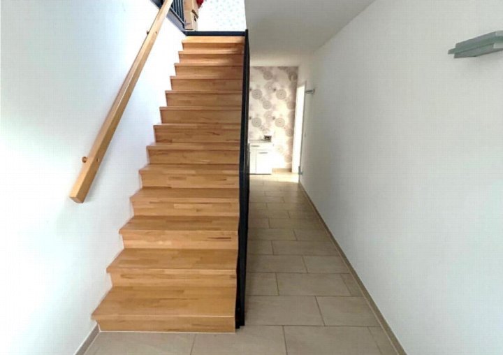 Holztreppe mit schwarzer Balustrade und Holzgeländer in einem Innenraum, Flur mit Fliesenboden im Hintergrund