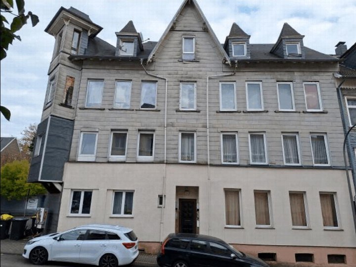 Fassade eines mehrstöckigen Wohnhauses mit Dachgauben, Fenstern und Eingangstür; vor dem Haus geparkte Autos; Lage in Langenfeld, Lärchenweg 44