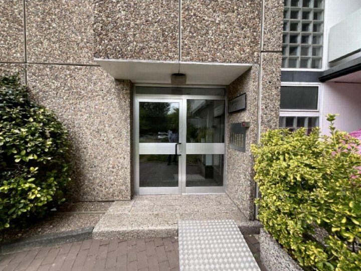Eingangsbereich eines Gebäudes mit Glastüren, granitartiger Fassade und bepflanzten Seitenbereichen in Bergisch Gladbach, Reginharstraße 2