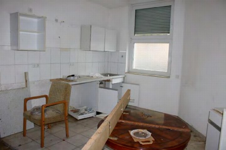 Küche mit weißen Fliesen, Schränken, Spüle und Fenster; Raum in Renovierungs- oder Leerstandszustand