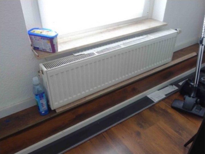 Innenraum mit Heizkörper unter Fensterbank, Holzboden und Gegenständen auf der Fensterbank