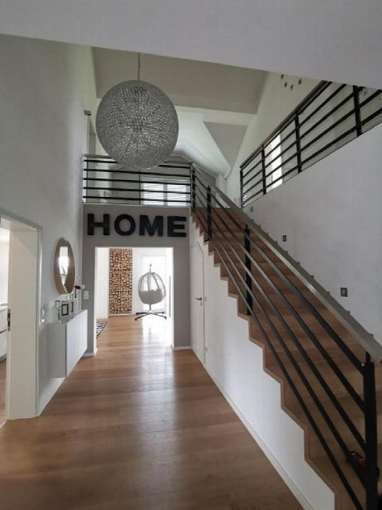 Treppenhaus mit Holztreppe, schwarzen Metallgeländern und runder Pendelleuchte. An der Wand steht das Wort 'HOME