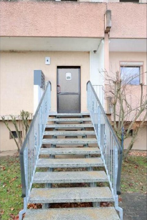 Eingangstreppe mit Metallgeländern zu einer Wohnungstür mit der Hausnummer 6, umgeben von Grünflächen und kahlen Sträuchern