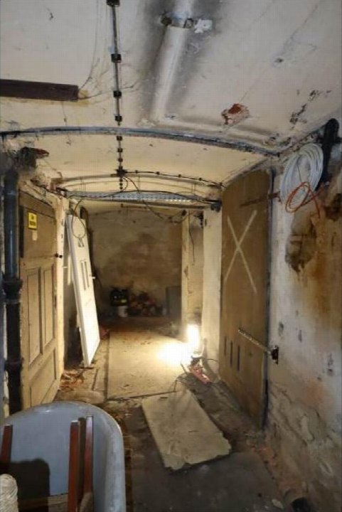 Dunkler, unrenovierter Keller mit Betonwänden, Rohrleitungen und einer Tür am Ende des Ganges in Görlitz