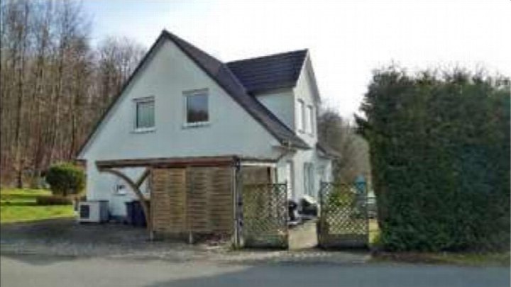 Einfamilienhaus mit weißer Fassade und dunklem Satteldach, Vorgarten und Holzabtrennung vor dem Eingangsbereich