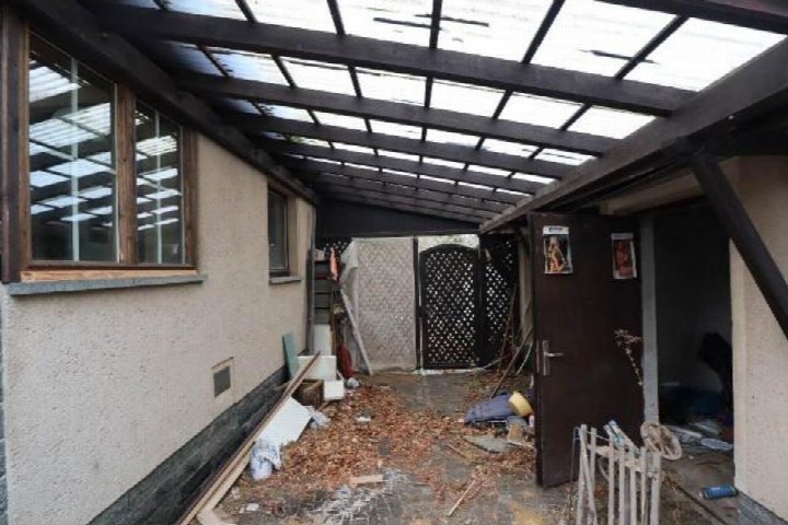 Gedeckter Eingangsbereich mit Glasdach, Holzrahmen und Tür; Boden mit Laub und Baustoffen bedeckt
