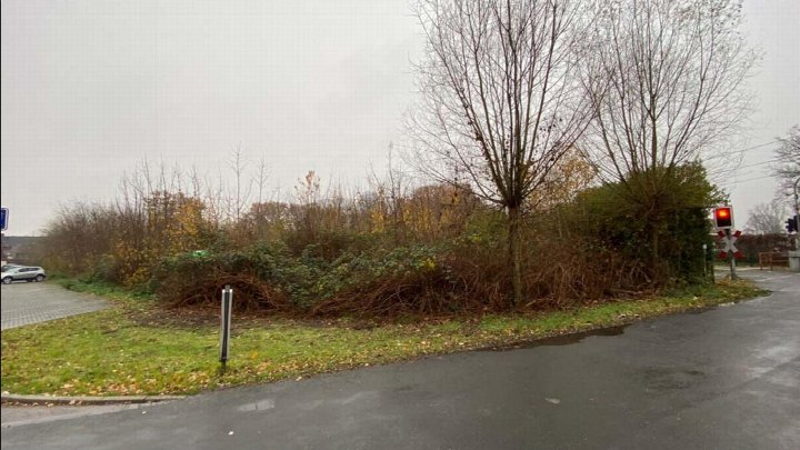Unbebautes Grundstück mit Grünfläche, Sträuchern und kahlen Bäumen an der Otterstraße in Dinslaken, neben einer Straße und einem Bahnübergang