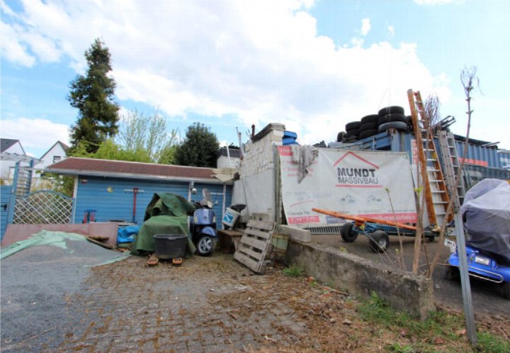 Hinterhof mit blauer Garage, geparktem Roller, Baustoffen und einem mit Plane abgedeckten Fahrzeug in Hürth