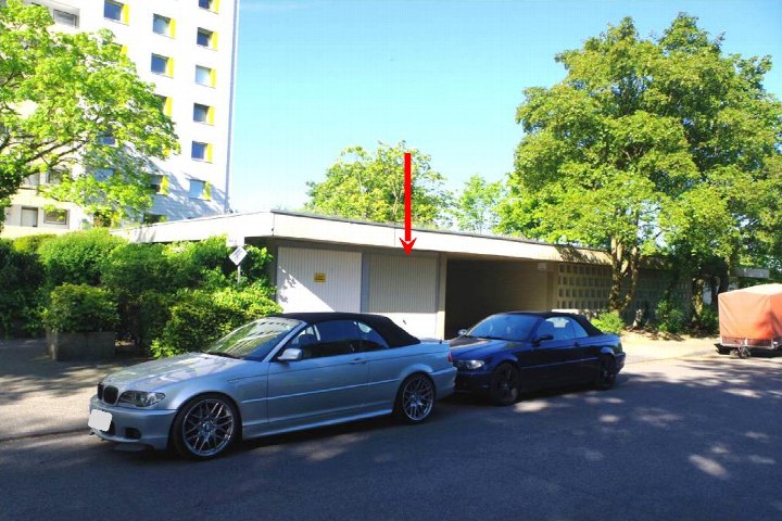 Zwei Cabriolets vor einer Garage mit Rolltor, umgeben von Bäumen und Sträuchern, im Hintergrund ein Wohngebäude
