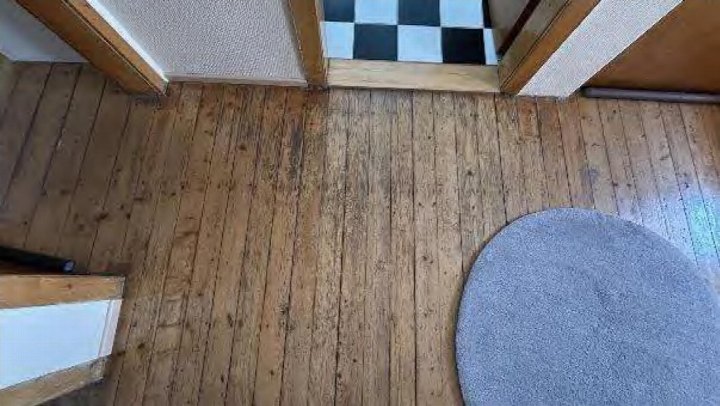 Holzboden im Wohnbereich mit runder grauer Teppichmatte und Türöffnung zu einem karierten Boden