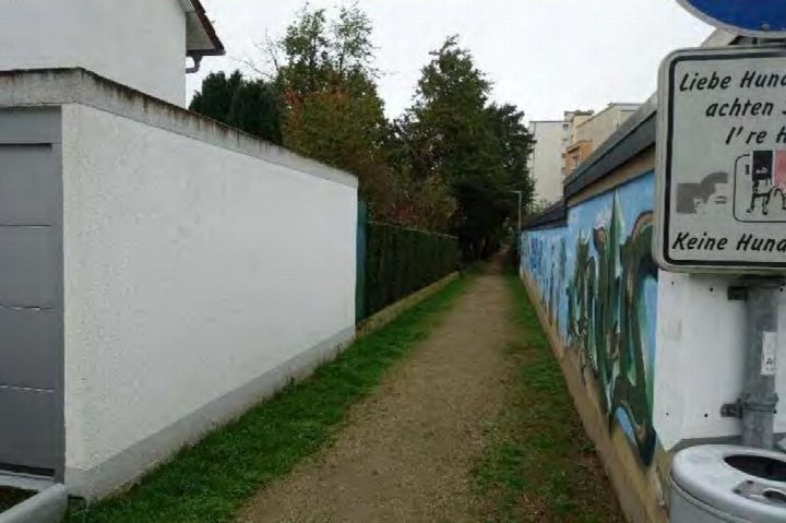 Narrower Weg zwischen Mauer und Grünfläche mit Hundekotstation und Wandmalerei, Teil eines Grundstücks in Kriftel