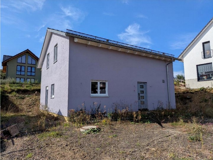 Seitenansicht eines Einfamilienhauses in Blankenheim, Graf-Hermann-Straße, mit lila Fassade, Fenstern, Tür und Dachgaube unter blauem Himmel