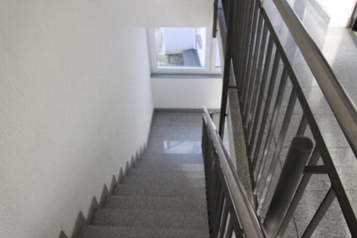 Treppenhaus mit grauen Stufen, weißer Wand und schwarzem Metallgeländer, Fenster im Obergeschoss
