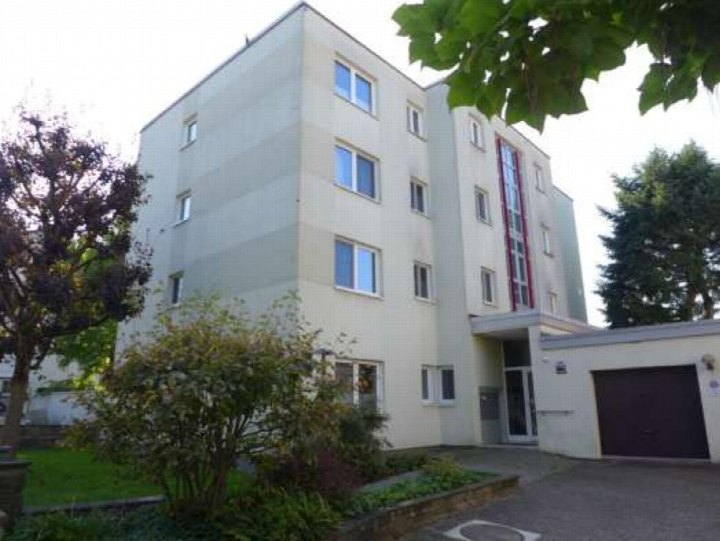 Vorderansicht eines Mehrfamilienhauses mit Eingang, Fenstern und angrenzendem Garten sowie Garage in Frankfurt am Main