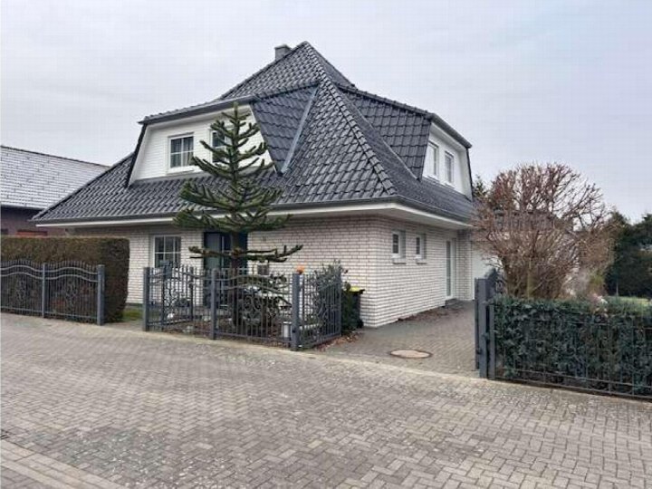 Einfamilienhaus mit Satteldach, weiß verputzter Fassade und dunklem Ziegeldach, Vorgarten mit Metallzaun und Tanne, Ansicht von vorne