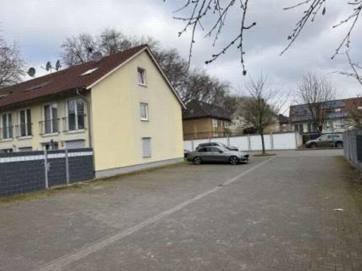 Pflasterplatz mit geparktem Auto neben einem gelben Reihenhaus mit dunklem Dach und dunkler Umzäunung in Duisburg, Marienstr. 44