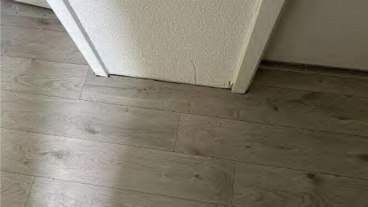Blick auf einen hellgrauen Holzoptikboden neben einer weißen Wand mit Putzstruktur im Innenraum eines Einfamilienhauses