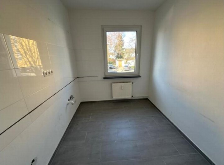 Leeres Badezimmer mit weißen Fliesen an der Wand, grauem Bodenbelag, Fenster und Heizkörper. Rödermark, Schillerstr. 19 B