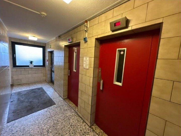 Treppenhaus mit roten Aufzugstüren, Fliesenwänden und Fenster im Erdgeschoss eines Wohngebäudes in Egelsbach