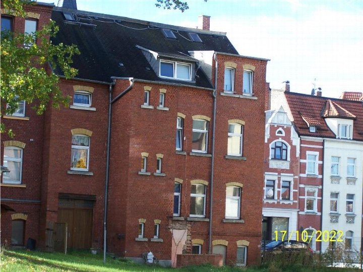 Seitenansicht eines mehrstöckigen Backsteinhauses mit Fenstern, Dachgauben und angrenzenden Gebäuden in Falkenstein