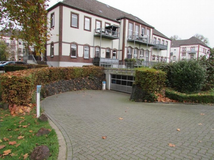 Garage-Eingang unter einem Mehrfamilienhaus mit gepflastertem Vorplatz und Hecke im Vordergrund