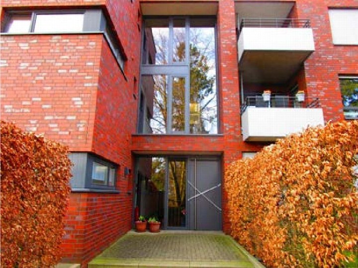 Eingangsbereich einer roten Backsteinwohnung mit Glastür, Stufen und herbstlichen Hecken an der Klosterstraße 18 in Stadtlohn