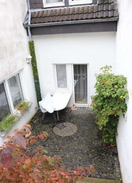 Gartenbereich mit Kopfsteinpflaster, Tisch, Stuhl und Pflanzen an den Wänden, Eingangstür im Hintergrund