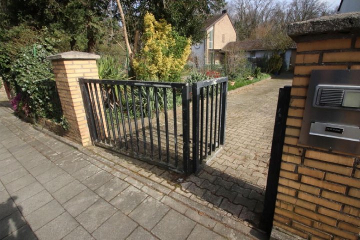 Eingangsbereich mit schwarzem Metalltor, Ziegelmauern und gepflastertem Weg zu einem Einfamilienhaus in Mönchengladbach