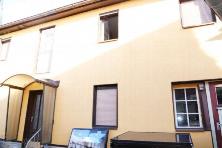 Gelbe Fassade eines Einfamilienhauses mit Eingang unter Bogenüberdachung, mehreren Fenstern und Dachanschluss