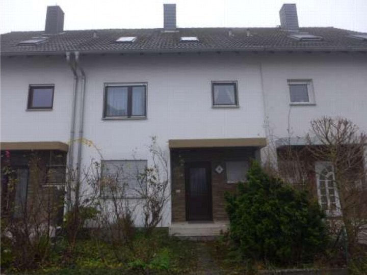Vorderansicht eines Einfamilienhauses mit weißer Fassade, dunklem Dach, Fenstern und Eingangstür, umgeben von Sträuchern und Garten