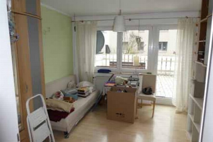 Wohnbereich mit Sofa, Kartons und Möbeln, Blick auf Balkon, hellgrüne Wand, Holzboden