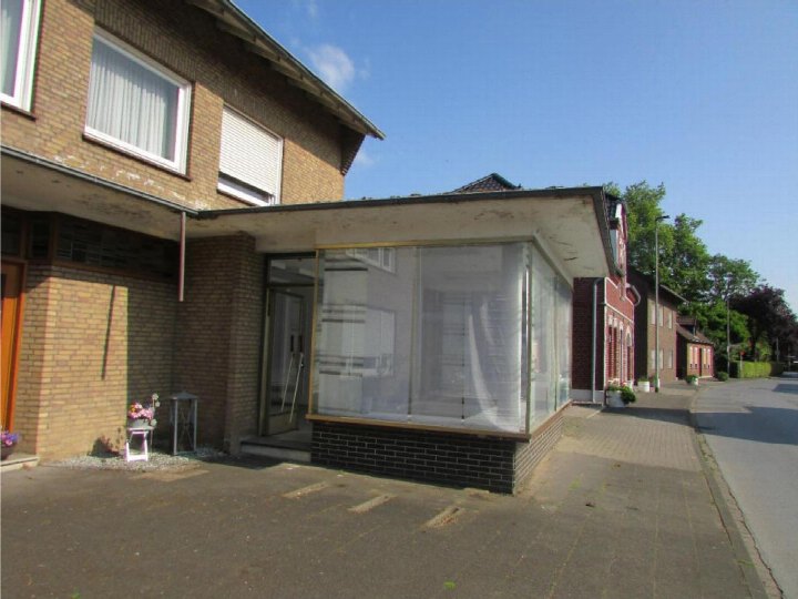 Außenansicht vorne eines Wohn-/Geschäftshauses in Wesel mit Eingang, Glasfront und Ziegelwand unter blauem Himmel