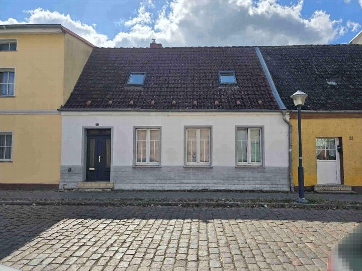 Vorderansicht eines Reihenhauses in Demmin, Kahldenwallweg 32, mit weißer Fassade, dunklem Ziegeldach und Eingangstür. Straßenpflaster im Vordergrund