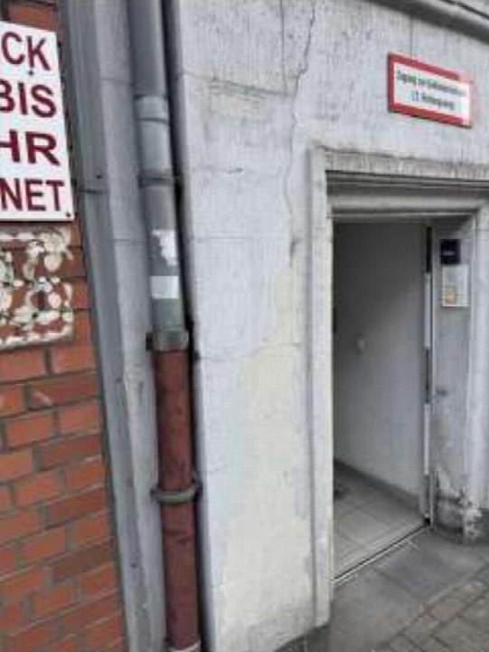 Eingangsbereich einer Eigentumswohnung mit Betonwand, Tür und Schildern, darunter ein rotes Schild mit Zugangshinweis