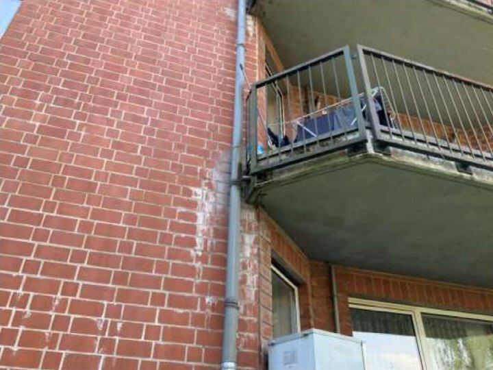 Balkon an einer roten Ziegelwand mit Metallgeländer und Wäsche im Hintergrund