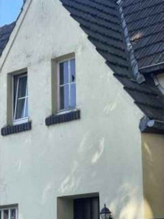 Seitenansicht eines Wohnhauses mit weißer Fassade, dunklem Satteldach und zwei Fenstern im Obergeschoss