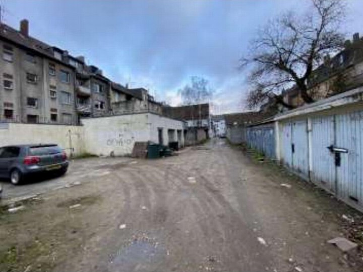 Dirtweg mit Garagen auf der rechten Seite und geparktem Auto links neben einem Mehrfamilienhaus in Duisburg