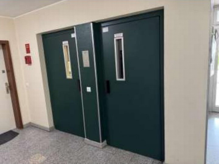 Innenansicht eines Flurs mit zwei dunkelgrünen Türen, Fliesenboden und Wandmontage von Feueralarmgeräten in einer Eigentumswohnung in Duisburg
