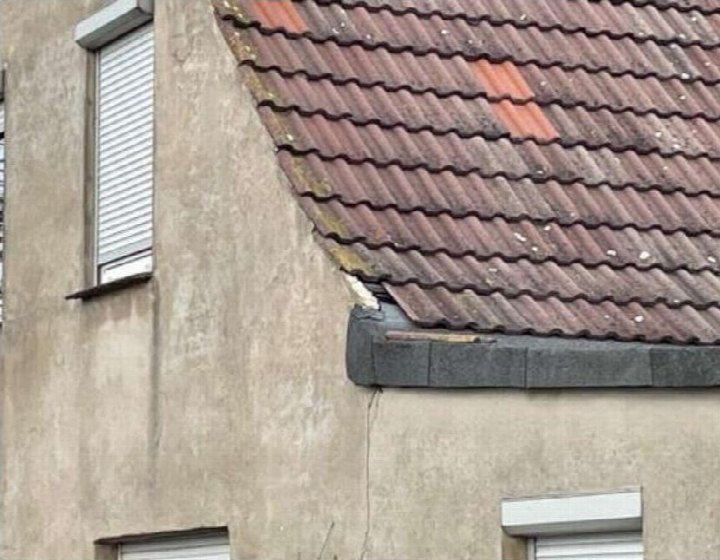 Dachansicht eines Einfamilienhauses mit Wellziegeln, teilweise mit Moosbewuchs und Fugenverschmutzung, sowie angrenzende Fassade mit Fenster