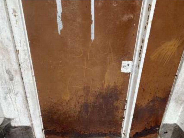 Rostige Metalltür in einem Kellerbereich mit Betonwänden und sichtbaren Verfärbungen