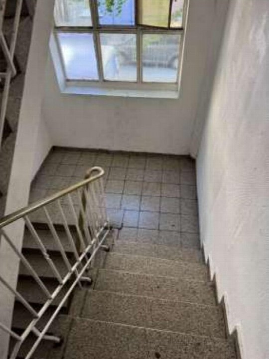 Treppenhaus mit Betonstufen, Metallgeländer und Fliesenboden, Fenster an der Wand oben