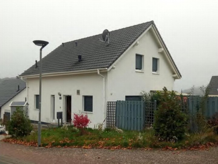 Einfamilienhaus in Schotten, Zum Eisenacker 15, mit weißer Fassade, grauem Dach und Vorgarten mit Büschen und Laub