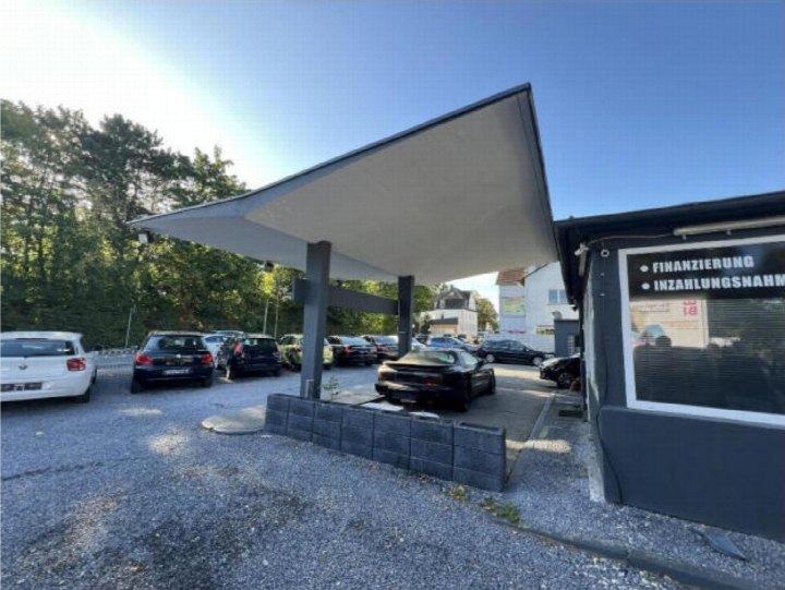 Parkplatz mit mehreren Fahrzeugen, Überdachung und Gebäude mit Schildern zur Finanzierung und Inzahlungnahme in Bielefeld