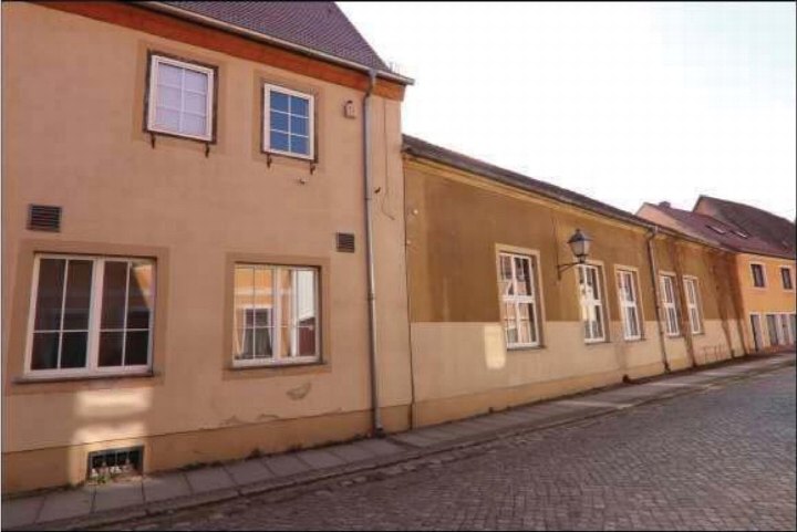 Seitenansicht eines mehrstöckigen Gebäudes mit Fenstern und Ziegeldach an einer Kopfsteinpflasterstraße in Mühlberg, Herrenstraße 23