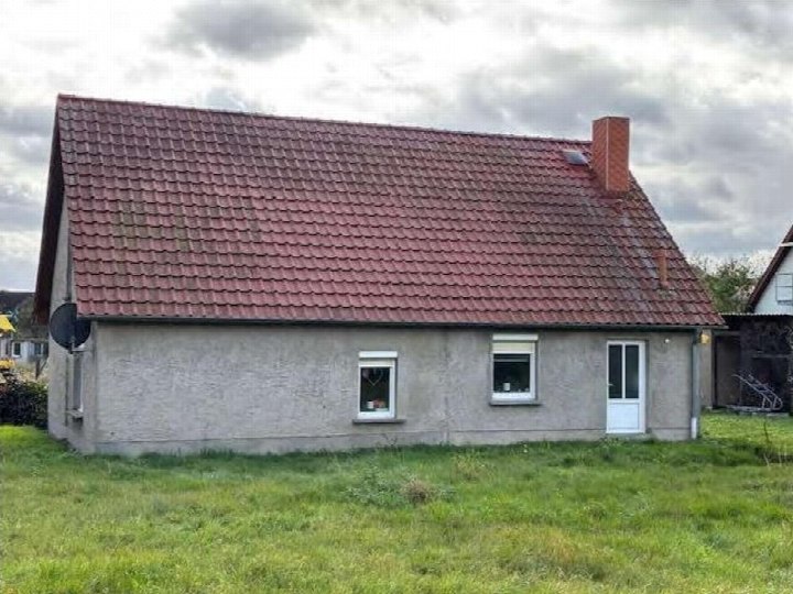 Seitenansicht eines Einfamilienhauses mit rotem Ziegeldach, grauer Fassade, Fenstern und Tür, umgeben von Grünfläche in Kastorf, Wolder Straße 29