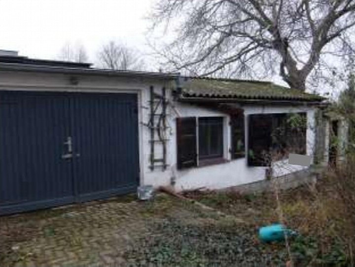 Garage mit blauen Toren an einem weißen Gebäude, daneben Gartenbereich mit kahlen Bäumen