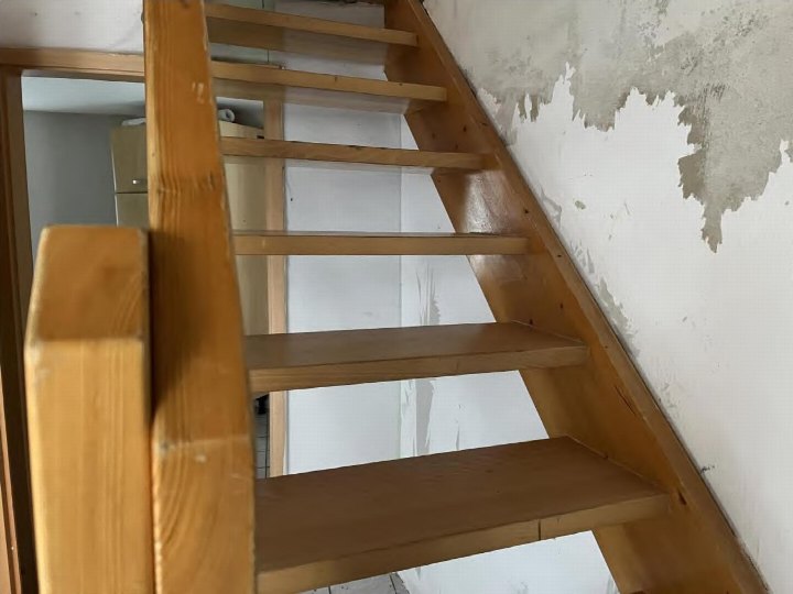 Holztreppe im Innenraum mit sichtbaren Stufen und Geländer, Wand mit abblätternder Farbe